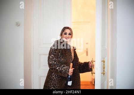 Bonne femme prête pour la fête du nouvel an.Jeune femme souriante attirante dans des vêtements de fête avec un maquillage pour les yeux fumés apportant une bouteille de champagne pour CH Banque D'Images