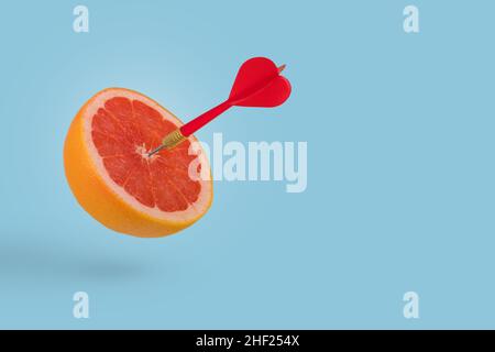 Tranche de pamplemousse, fruit avec cible circulaire marquée et dart rouge sur fond bleu vif.Idée minimale de nourriture et de fruits concept.idée créative à produ Banque D'Images