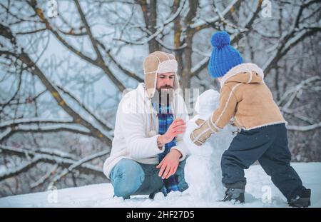 Bonne famille se plaquant avec un bonhomme de neige.Fête des pères.Père et son fils jouant à l'extérieur.Scène d'hiver sur fond de neige blanche. Banque D'Images