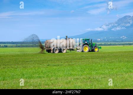 Un gros tracteur qui épandre de l'engrais pour améliorer la récolte sur les pâturages ou les champs dans les hautes montagnes de Tatra.Concept d'agriculture terrestre.Janvier 2022, Poprad, Slovaquie. Banque D'Images