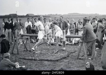 Vintage image ou Black and White Photograph ou spectateurs et joueurs dans un jeu de combat de pilow traditionnel sur le faisceau de bois joué dans un camp de vacances anglais dans l'Angleterre 1930s Banque D'Images