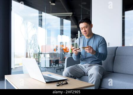 anxieux asiatique essayant de faire le paiement en ligne par carte de crédit et téléphone, homme d'affaires travaillant dans le bureau, erreur de demande de banque Banque D'Images