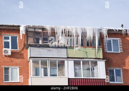 Balcons d'une ancienne maison résidentielle en brique couverte par les immenses glaçons.Des glaçons dangereux pendent du toit.Difficile nord hiver dans la ville. Banque D'Images