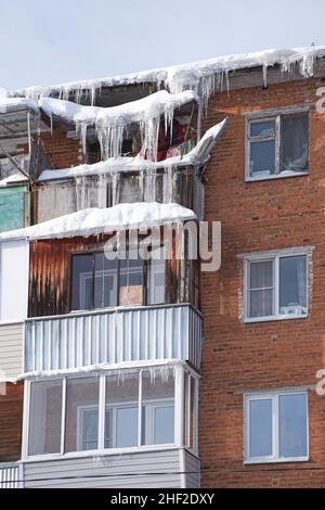 Balcons d'une ancienne maison résidentielle en brique couverte par les immenses glaçons.Des glaçons dangereux pendent du toit.Difficile nord hiver dans la ville. Banque D'Images