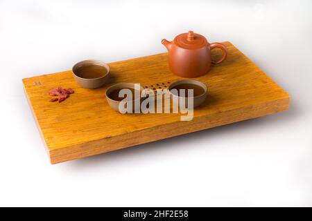 Théière en céramique et trois tasses traditionnelles pour boire du thé oriental sur une table en bois pour les cérémonies du thé sur fond blanc.Les tasses sont remplies de wi Banque D'Images