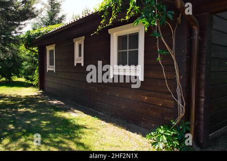 Simple cottage en bois sombre à la belle journée d'été.Le mur de la maison d'hôtes avec trois fenêtres.Vacances, week-end, loisirs nature. Banque D'Images