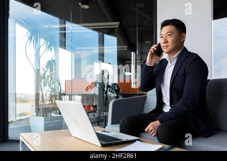 Pensant homme d'affaires asiatique, parlant au téléphone dans un bureau moderne, à l'écoute sérieusement Banque D'Images