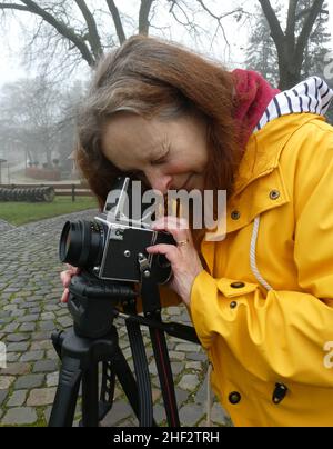 Les anciens appareils photo sont amusants !Une photographe féminine exploite un appareil photo à pellicule de format moyen à un œil du 1980s.L'appareil photo SLR est posé sur un trépied. Banque D'Images