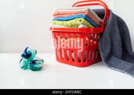 Les serviettes multicolores sont dans un panier à linge rouge sur fond blanc.Lavage et repassage des vêtements, vue du dessus Banque D'Images