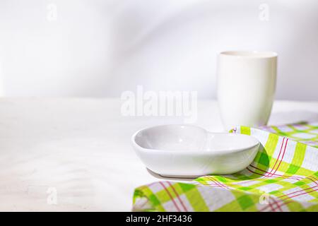 Bol en céramique blanche en forme de coeur avec tasse, les plats vides sont mis pour le petit déjeuner sur une surface de cuisine en pierre blanche, gros plan, foyer sélectif Banque D'Images