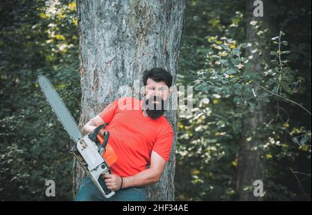 Bûcherons.Jeune homme élégant qui se pose comme un bûcheron.Travailleur de bûcherons marchant dans la forêt avec une tronçonneuse.Bûcheron tenant le Banque D'Images