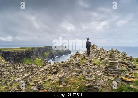 Homme debout entre des promenades en pierre et admirant la vue sur les falaises emblématiques de Moher, attraction touristique populaire, Wild Atlantic Way, Co. Clare, Irlande Banque D'Images