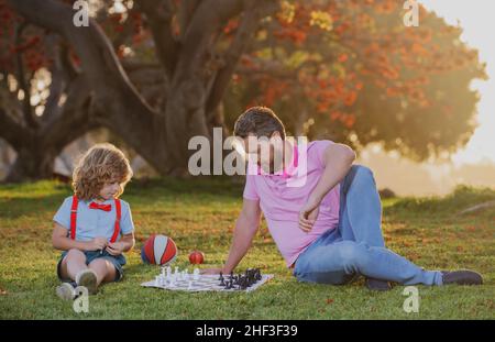 École d'échecs pour enfants.Père et fils jouant aux échecs allongé sur l'herbe au parc de pelouse.Fête des pères, famille d'amour, parentalité, concept d'enfance.Enfant concentré Banque D'Images