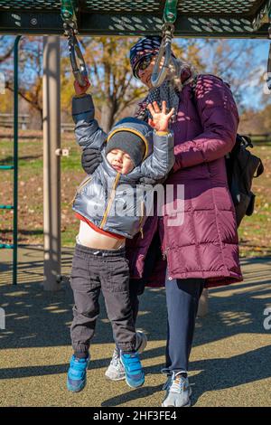 Grand-mère aidant un garçon de deux ans à pendre de l'équipement de terrain de jeu du parc de la ville Banque D'Images