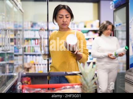 Femme latino-américaine qui choisit des produits laitiers dans une épicerie Banque D'Images