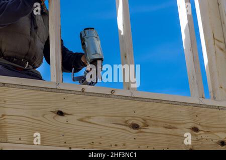 Constructeur en clouant des poutres en bois travaille pour la construction à l'aide d'un marteau pneumatique Banque D'Images