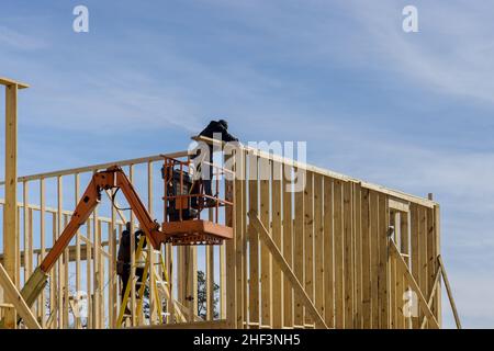 Gros plan d'un travailleur en tenant une planche à poser sur la construction de maison à l'aide d'un marteau pneumatique dans des poutres en bois cloutées. Banque D'Images