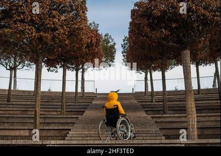 Femme en fauteuil roulant devant les escaliers dans la rue en hiver. Banque D'Images