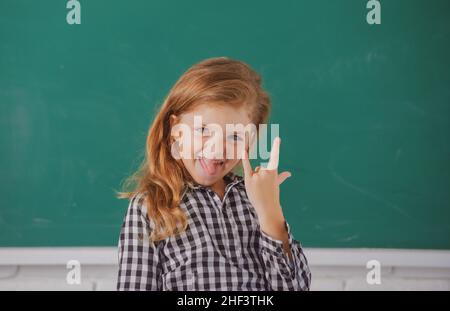 Portrait de drôle de fille élève de l'étude primaire.Petite fille drôle à l'école.Enfant de l'école primaire en classe.Langue amusante Banque D'Images