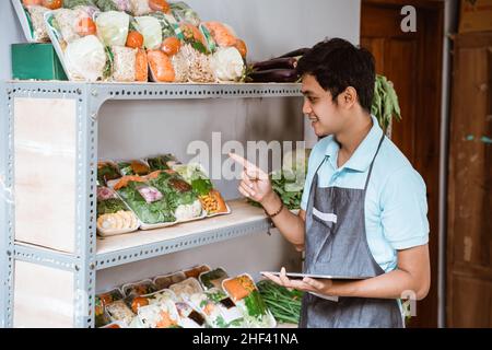 Homme vendant des légumes comptant des légumes à l'aide d'une tablette numérique Banque D'Images