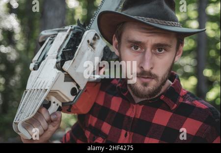 Thème de l'agriculture et de la foresterie.La journalisation illégale se poursuit aujourd'hui.Un beau jeune homme avec une barbe porte un arbre.Bûcherons. Banque D'Images