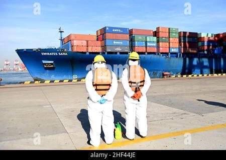 QINGDAO, CHINE - le 14 JANVIER 2022 - les Dockers attendent de fixer les câbles et de désinfecter les câbles aux navires de fret au quai entièrement automatisé du port de Qianwan Banque D'Images