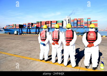 QINGDAO, CHINE - le 14 JANVIER 2022 - les Dockers attendent de fixer les câbles et de désinfecter les câbles aux navires de fret au quai entièrement automatisé du port de Qianwan Banque D'Images