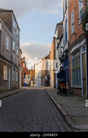 Homme poussant un buggy dans Wormgate, une vieille rue pavée à l'arrière de l'église de souche. Banque D'Images