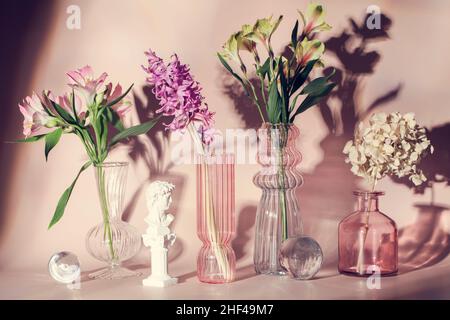 Fleurs fraîches dans des vases sur fond beige. Objets en verre de couleur tendance.Encore la vie, l'art, l'amour concept.Style botanique.Photo pour carte de vacances. Banque D'Images