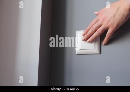 Une belle main féminine appuie sur le commutateur au mur Banque D'Images