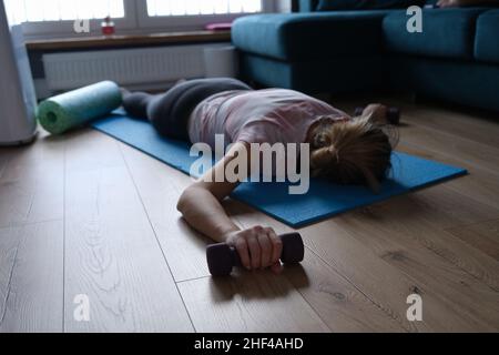Une femme de sport fatiguée avec des haltères se trouve sur le sol Banque D'Images