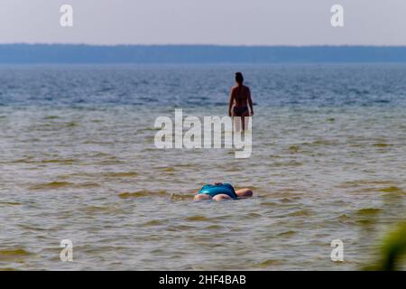 Femme en surpoids en maillot de bain allongé dans une eau.Vacances sur la plage du lac. Banque D'Images