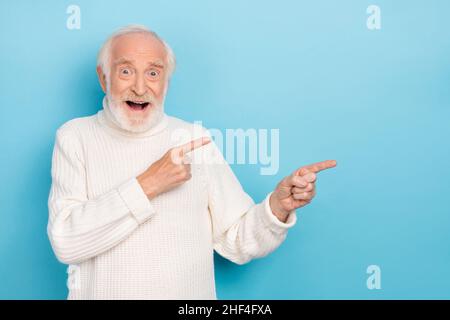 Photo de l'homme de cheveux gris plus âgé impressionné indiquer promo porter chandail blanc isolé sur fond bleu Banque D'Images