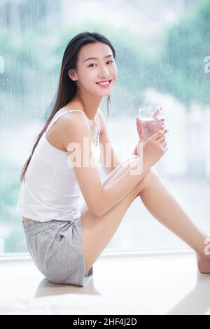 Jeune femme assise sur le seuil de la fenêtre et de l'eau potable Banque D'Images