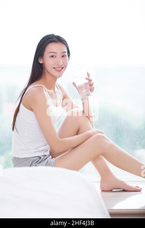 Jeune femme assise sur le seuil de la fenêtre et de l'eau potable Banque D'Images