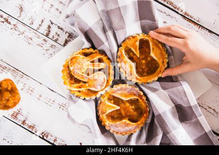 Les enfants prennent main une tartelette arrosée de sucre en poudre avec de la confiture de pêche.Décoration de Pâques.Ci-dessus Banque D'Images