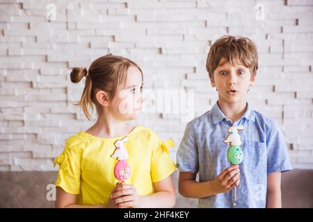 Adorable fille et garçon souriant tenant un pain d'épice fait main coloré sur un bâton le jour de Pâques Banque D'Images