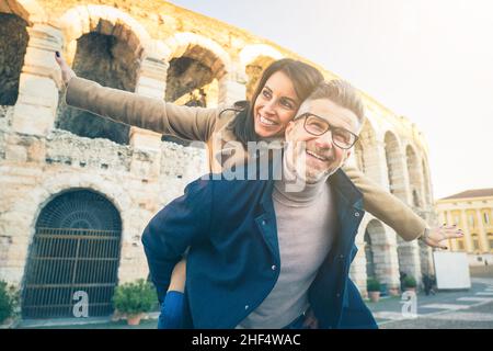 Heureux couple senior dans l'amour s'amuser en face du célèbre monument de l'Italie.Vue en contre-angle d'une femme gaie qui s'étire les bras tout en étant assise Banque D'Images