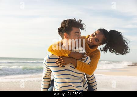 Homme biracial donnant une bonne petite amie promenade en pigeyback à la plage contre le ciel par jour ensoleillé Banque D'Images