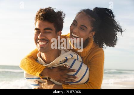 Joyeux biracial homme donnant le pigeyback à la petite amie à la plage le jour ensoleillé Banque D'Images