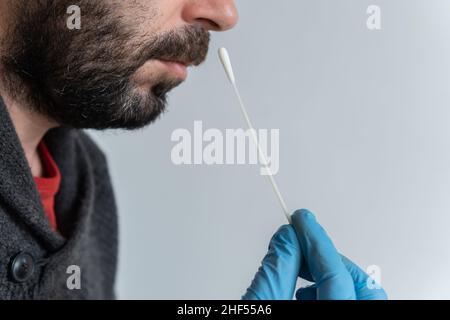 Gros plan d'un homme caucasien brun avec barbe, effectuant un test d'antigène avec un gant médical bleu en nitrile Banque D'Images