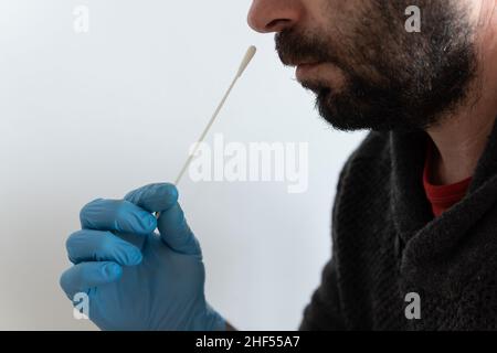 Gros plan d'un homme caucasien brun avec barbe, effectuant un test d'antigène avec un gant médical bleu en nitrile Banque D'Images