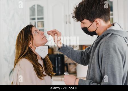 Jeune homme prenant écouvillon du nez de mère à la maison Banque D'Images