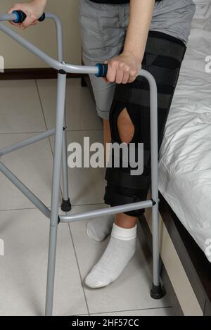 Femme portant un étrésillon de jambe après une intervention chirurgicale sur une fracture du genou essayant de marcher avec un marcheur.Réadaptation après une blessure.Gros plan Banque D'Images