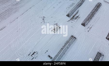 Vol sur un terrain enneigé.Les balles de paille sont empilées.Des traces de labour agricole sont visibles sous la neige.Photographie aérienne. Banque D'Images