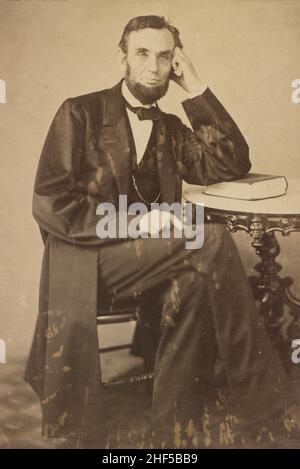 Abraham 'Abe' Lincoln 1809-1865.La photographie montre un portrait complet de Lincoln assis à une table et pendu sur un livre.Août 1863. Banque D'Images
