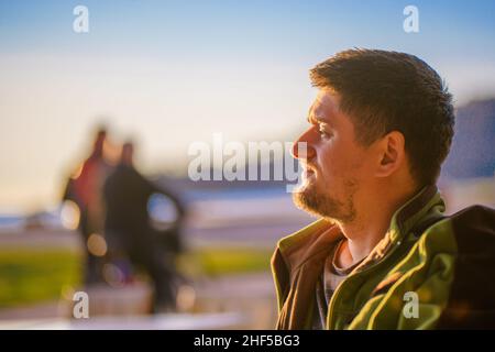 Beau jeune homme en profil rapproché.Un touriste bénéficie d'un coucher de soleil lumineux sur la côte de la mer d'hiver. Banque D'Images