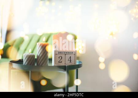 Date de la veille de Noël.Décembre 24 sur calendrier en bois debout sur une petite table avec des bougies allumées dans le salon, foyer sélectif.Noël et New Yea Banque D'Images