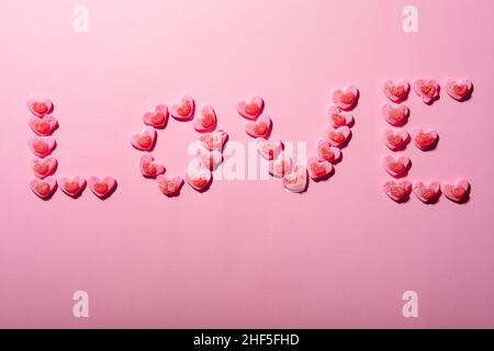 Texte d'amour fait de bonbons en forme de coeur isolé sur fond rose, espace de copie Banque D'Images