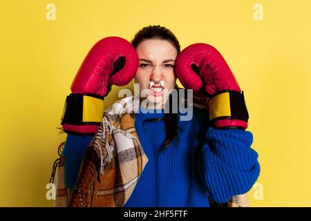 Portrait de la jeune femme caucasienne grippe et rhume, se sentant malade portant des gants boxeurs isolés sur fond jaune studio. Banque D'Images